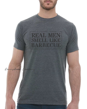 This design features a rustic font that reads "Real Men Smell Like Barbecue" Everyday lightweight smooth & comfy tee.  (Slim Fit). Available in Blue/Green/Grey/Brown